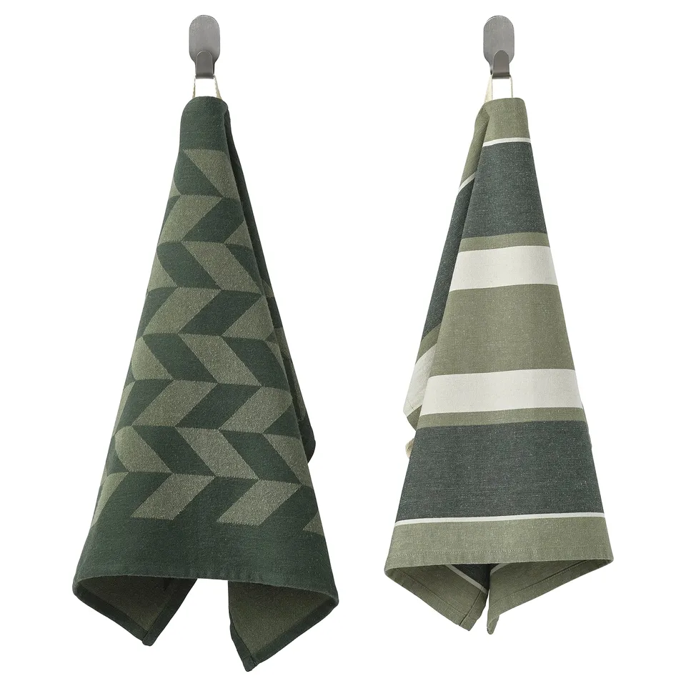 Two green kitchen towels hang, one geometric, one striped, both cotton and jute.