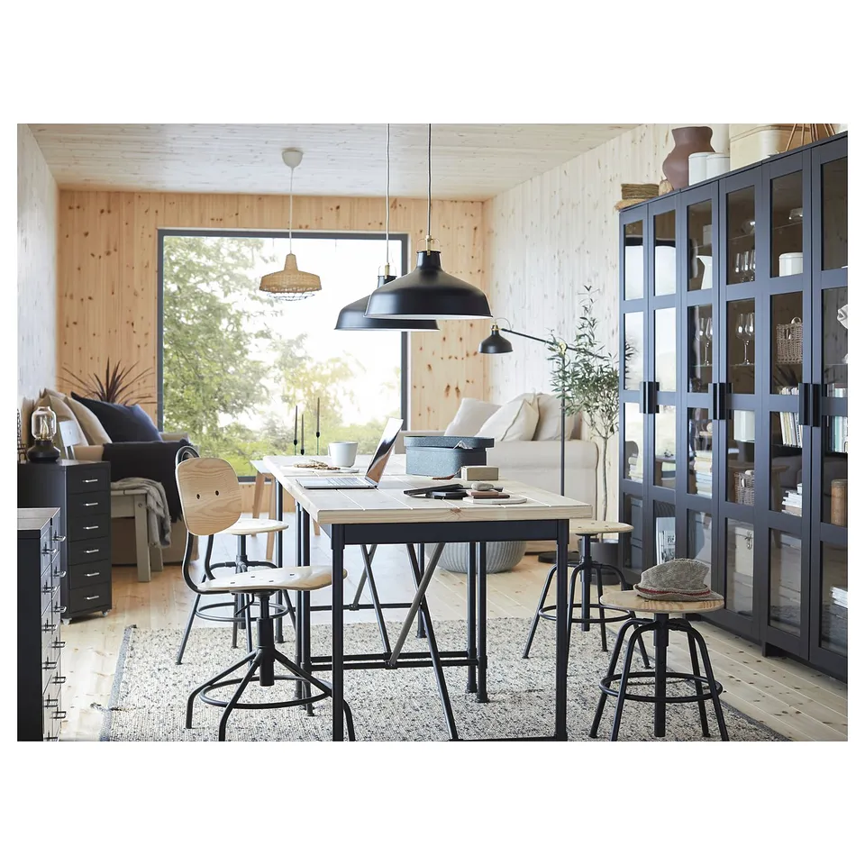 Modern open-plan living space featuring KULLABERG black desk, black pendant lamps, and white couch. Large window reveals greenery.