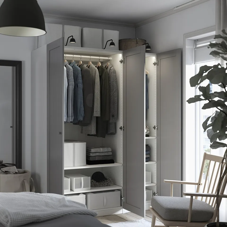Modern bedroom with open grey wardrobe displaying clothes, shelves with storage boxes, and integrated lighting.