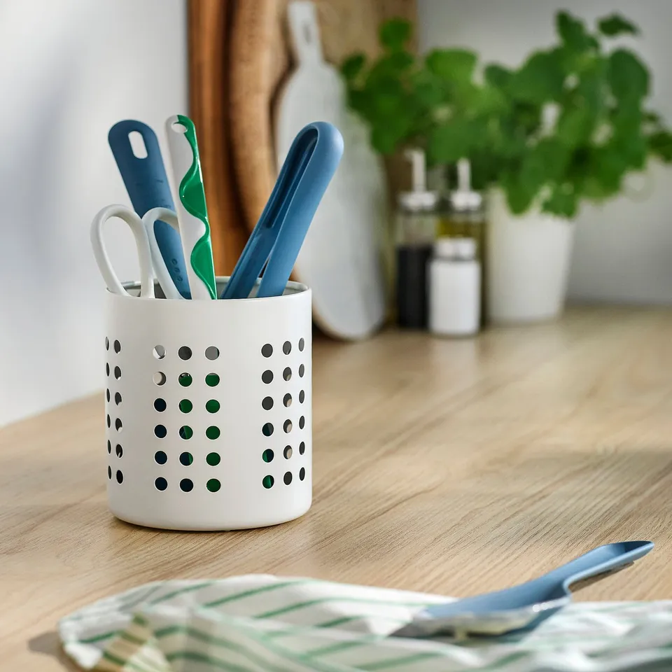 White cutlery holder with tools on wooden table.