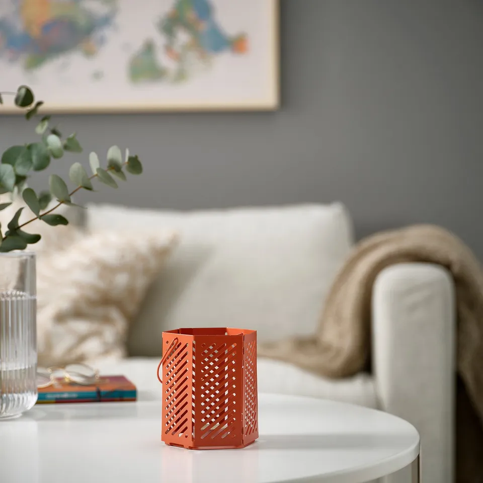 Red metal lantern on white table beside couch. Patterned design casts shadows on walls. Size similar to stack of books.