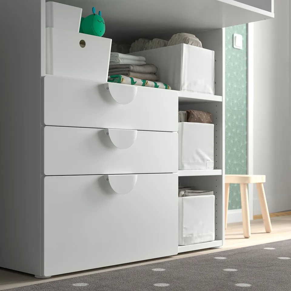 White SMÅSTAD storage unit with drawers, holding folded textiles and various items in a room. A drawer stop for safety.