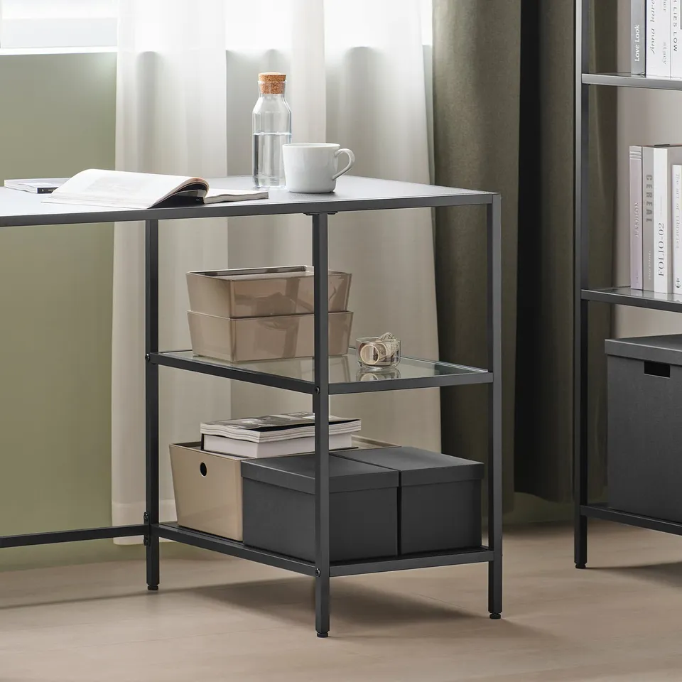 Three-tier metal and glass storage shelf with boxes, books, and a mug. The middle shelf holds a camera.