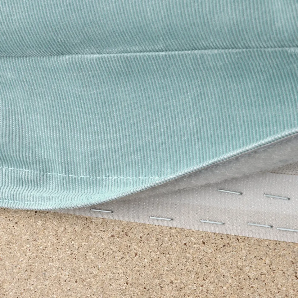 Close-up of washable, light blue VIMLE sofa fabric with white stitching, laid on cork surface.