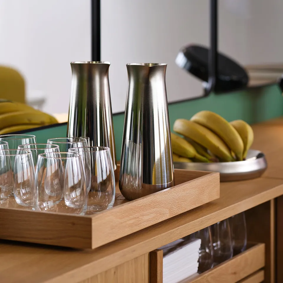 Modern metallic carafe and glass set on wooden tray, perfect for serving cold drinks. Ideal for minimalist decor, combining style with functionality.