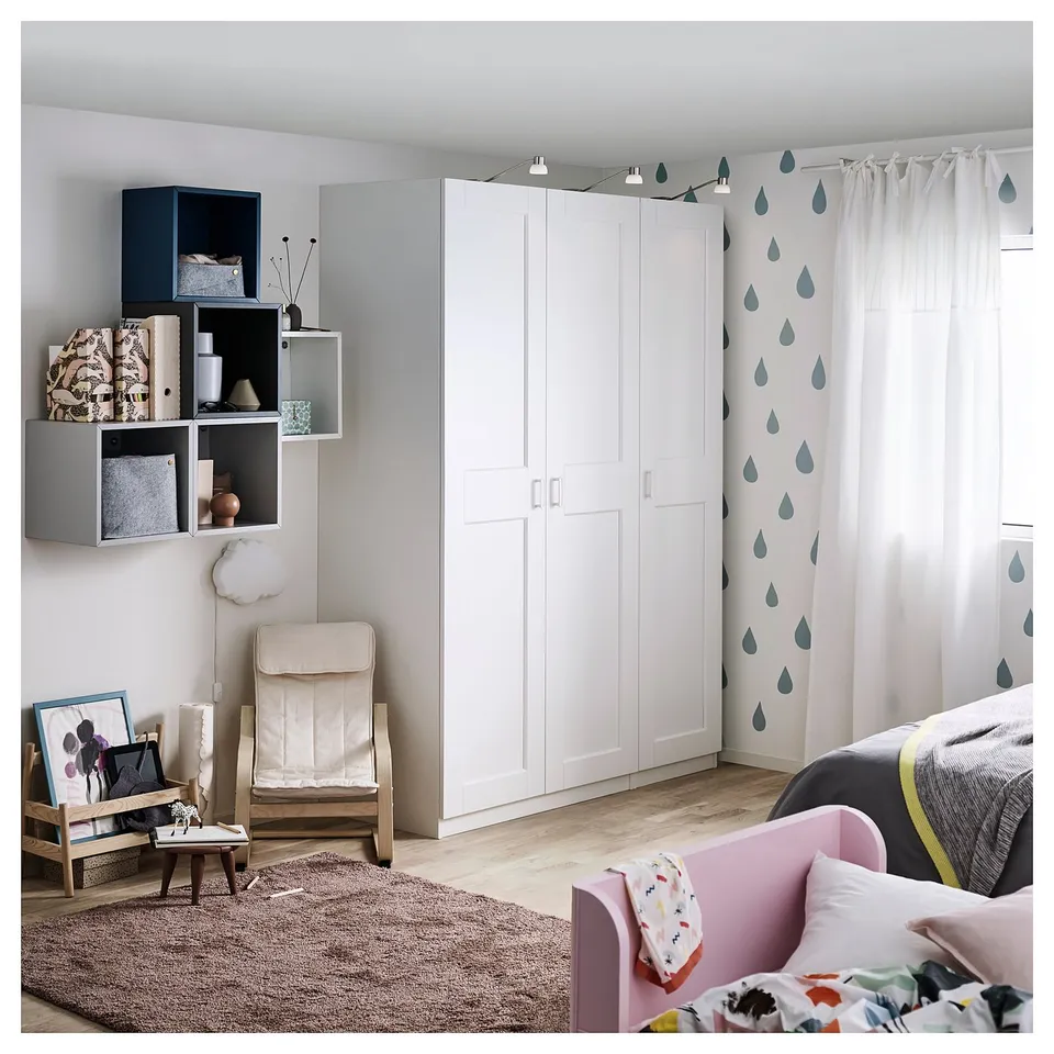 Modern kids bedroom with white wardrobe, shelves, and playful raindrop curtains. Light pink bed, patterned rug, and various decorative items.
