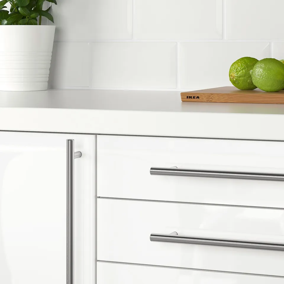 Modern kitchen with white cabinets and metallic handles. A white countertop holds a plant and limes.