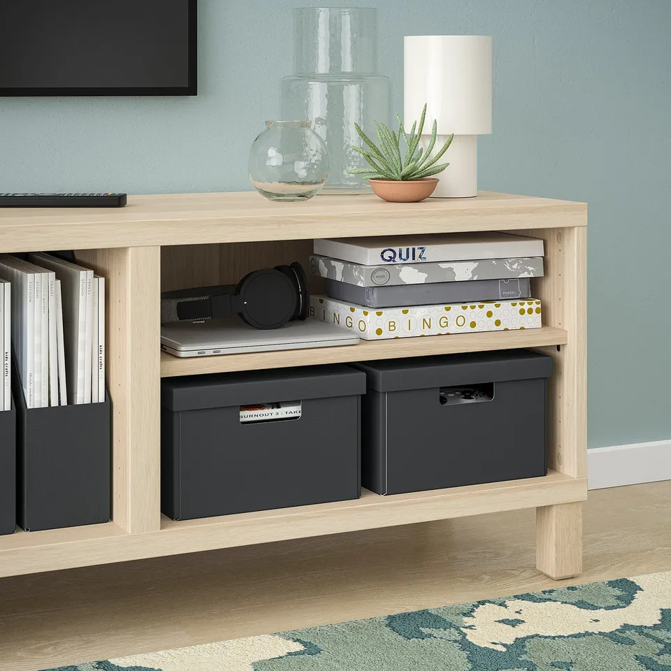 Wooden tv stand with books, boxes, plant, laptop, headphones, lamp, and vases.