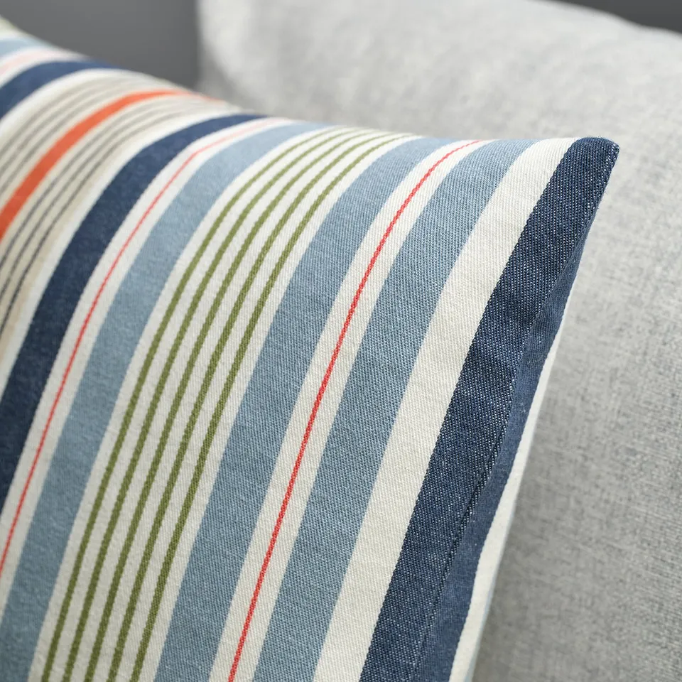Striped pillow with blue, red, green, and white lines on a grey fabric background. Hidden zip, soft yet textured feel.