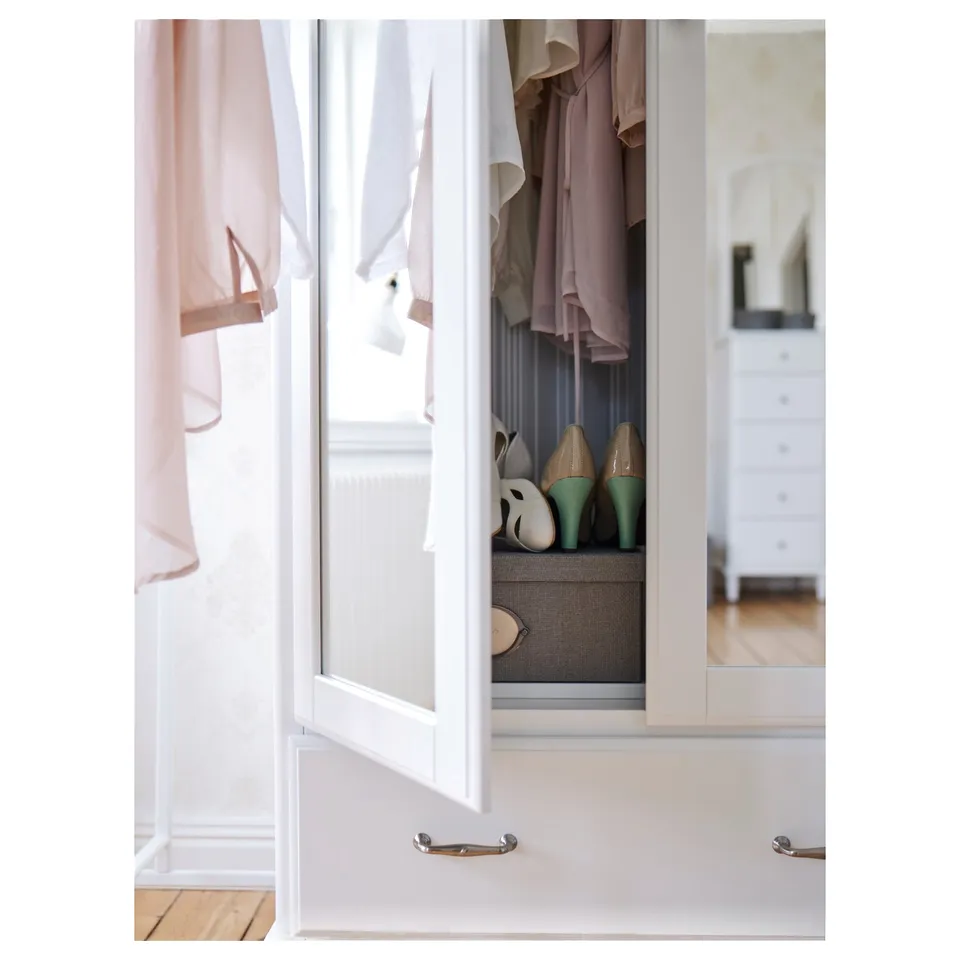 Open white closet door revealing clothes and shoes, with pastel pink curtains.