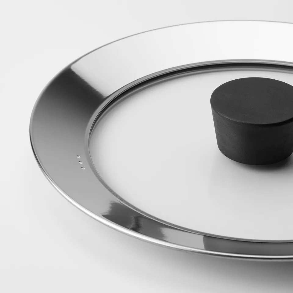 Close-up of KLOCKREN glass lid with metal rim, black handle, clean design.
