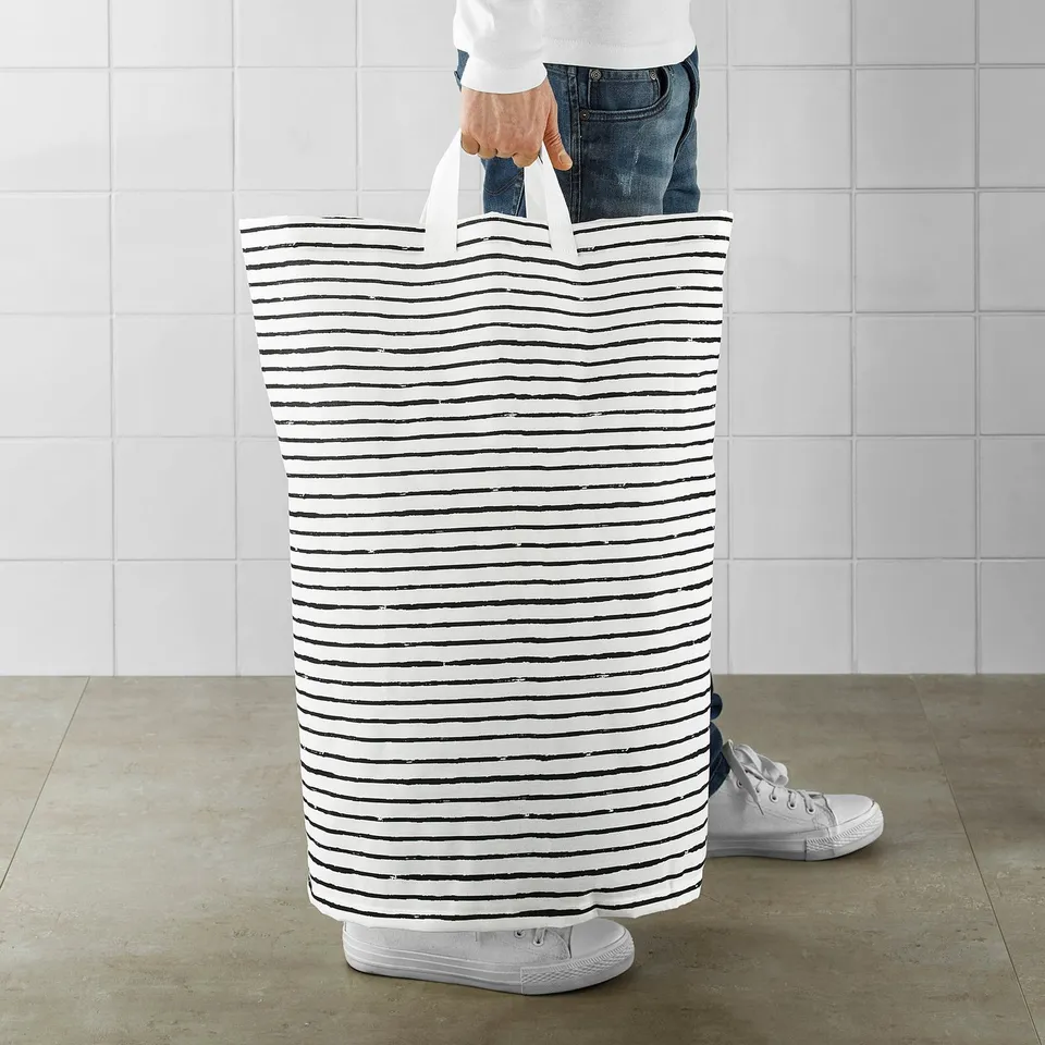Person holding a tall striped laundry bag, standing upright on the floor.