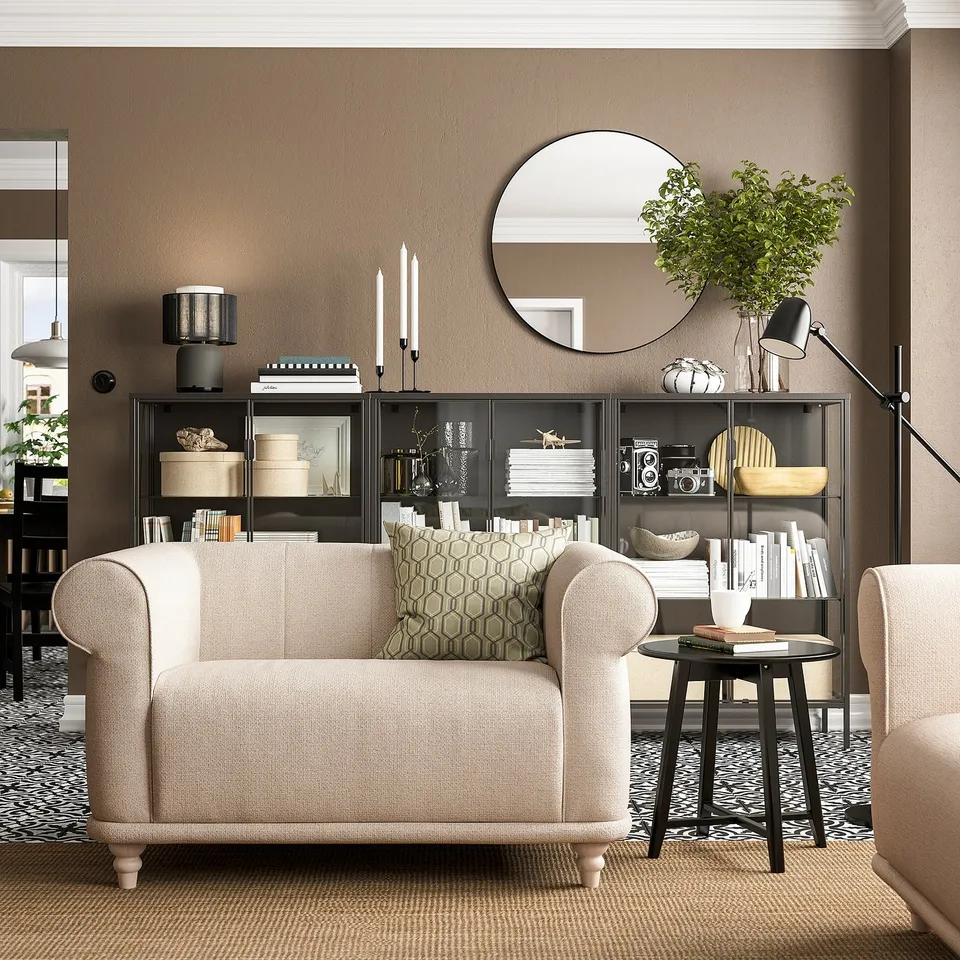 Cosy living room with beige VISKAFORS armchair, patterned cushions, black side table, and shelves with decor and plants.