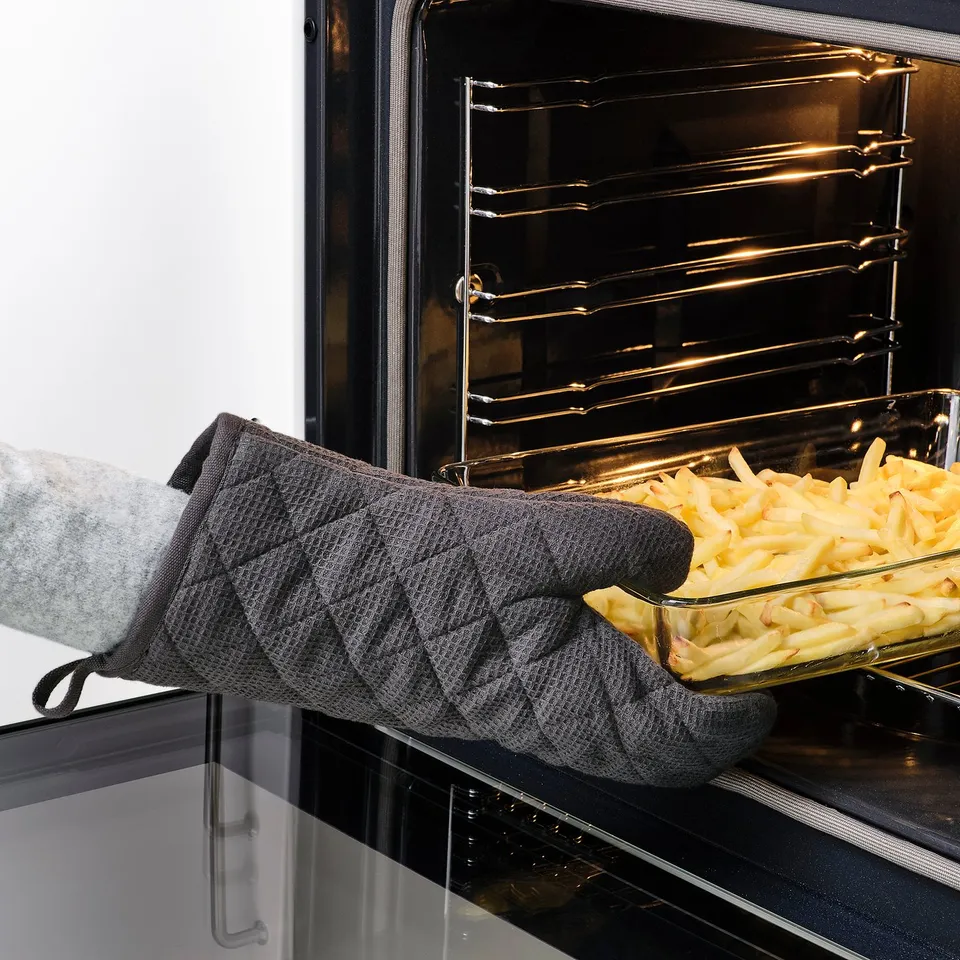 Person putting dish in oven wearing RINNIG gloves for heat protection.