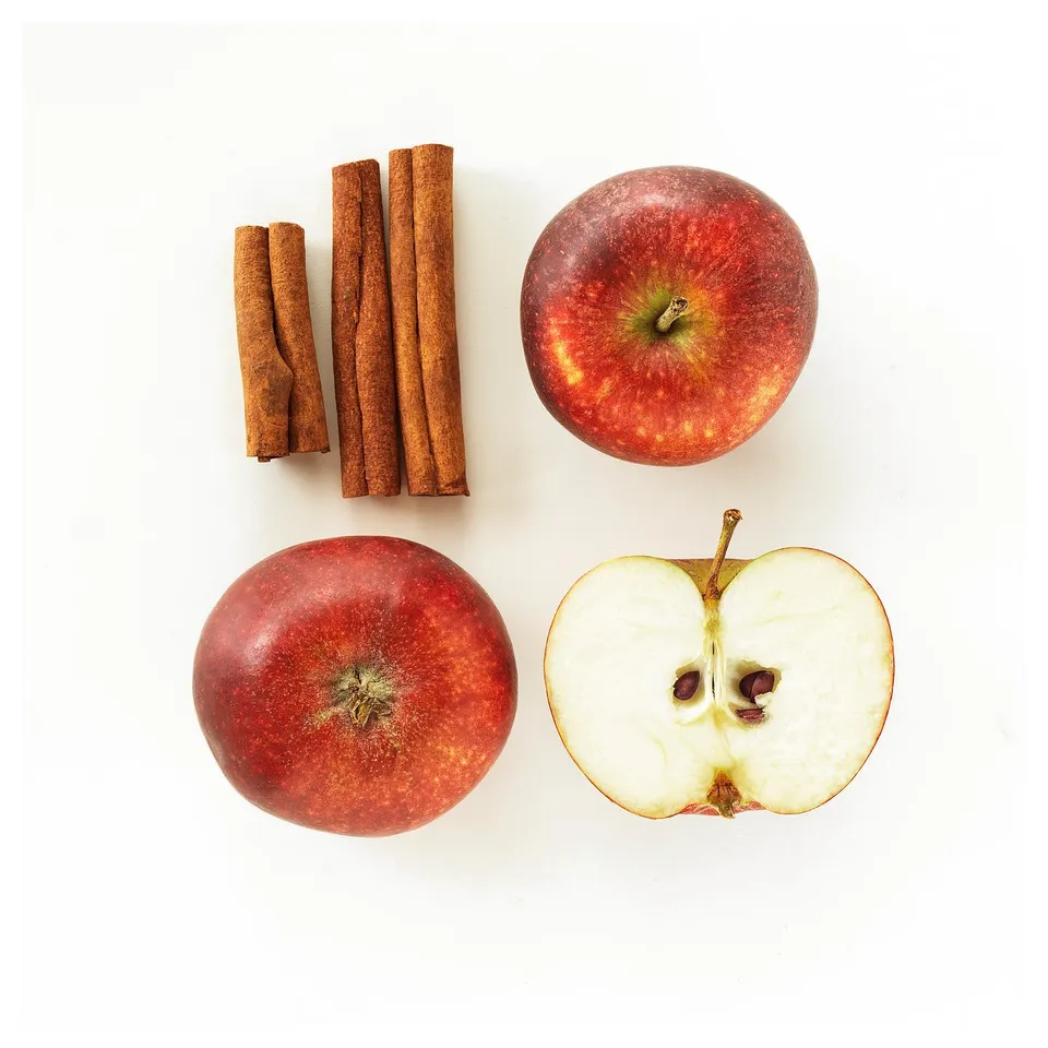 Red apples and cinnamon sticks, one apple sliced, white background.