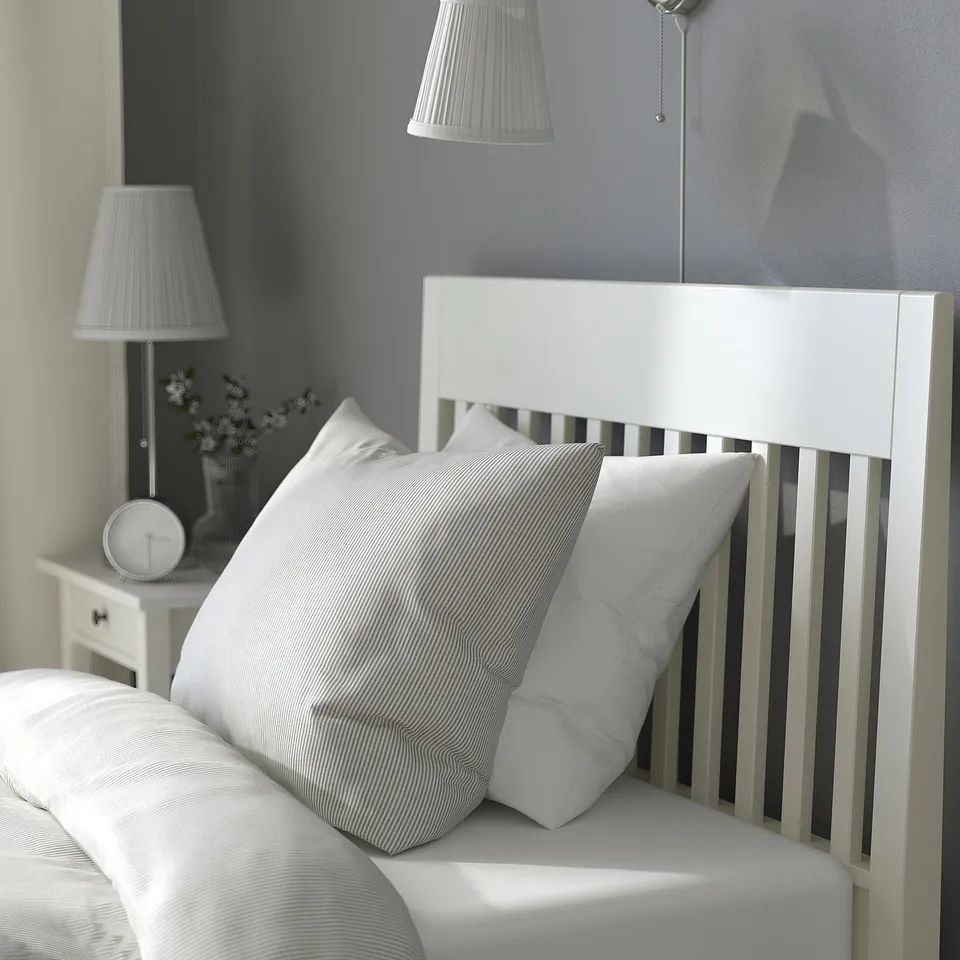 Minimalist bed with striped pillows and bedside table with lamp and clock.