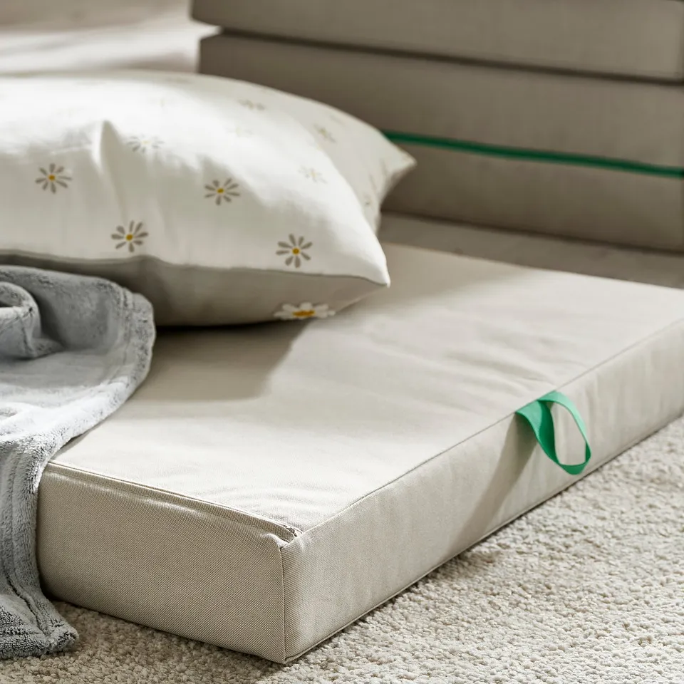 Soft, folded kids foam mattress on carpet, with decorated pillows and grey blanket, ready for play or rest.