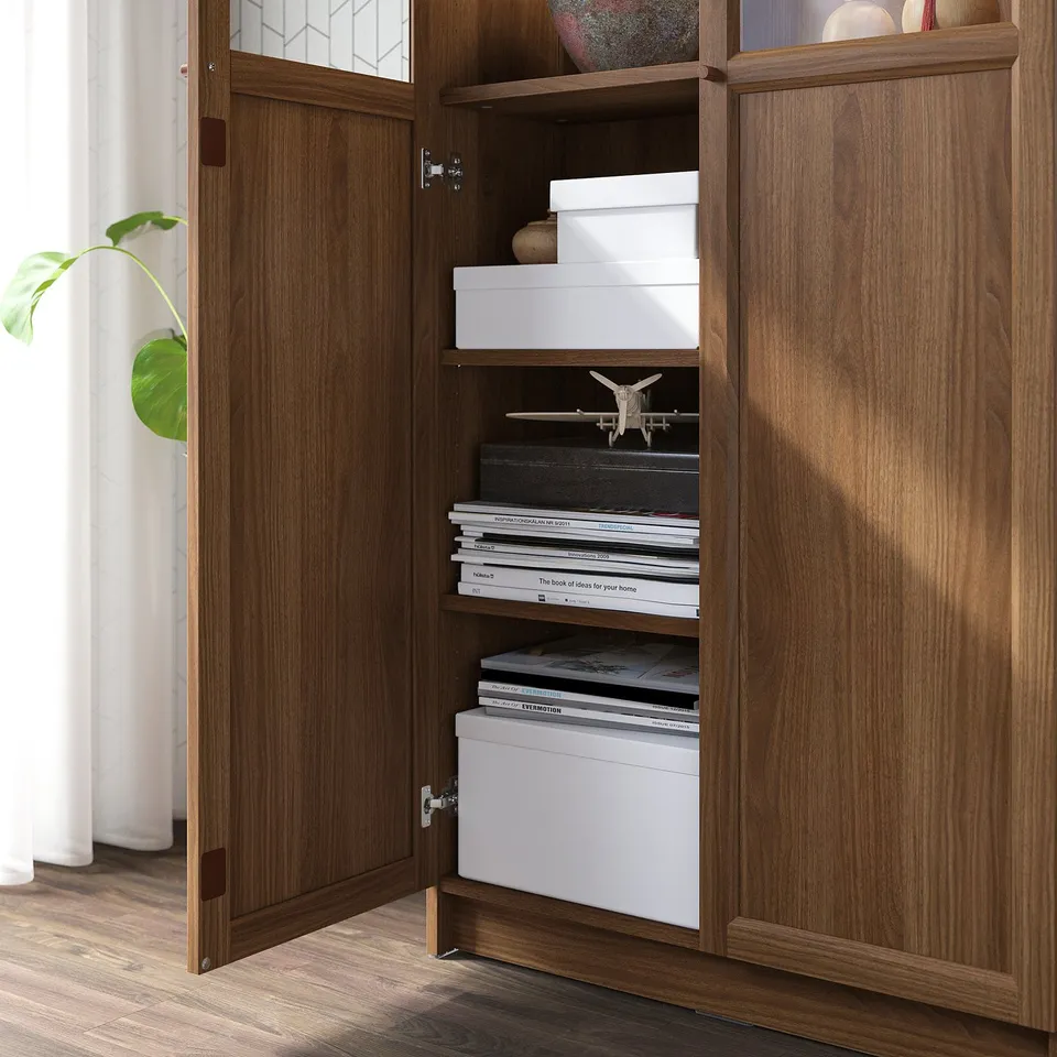 Wooden cabinet with multiple shelves holding books and white storage boxes. One door is open, revealing organised storage.