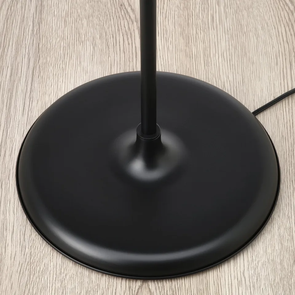 Base of minimalist floor lamp, sturdy black metal stem rising from solid circular base, on wooden floor.