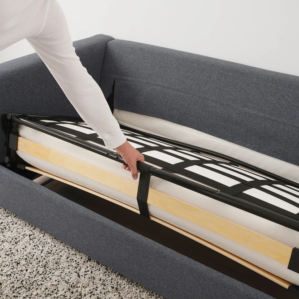 Person pulling out sofa bed mattress, revealing black metal frame and wooden slats.