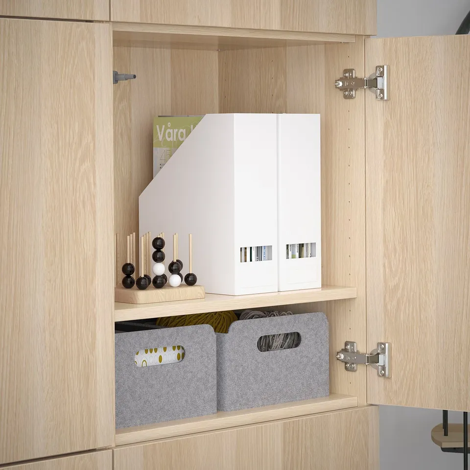 Light wooden cabinet with adjustable shelves holding storage boxes and a magazine.