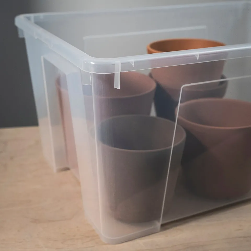 Clear plastic storage bin with four clay pots inside, demonstrating durability and visibility for organised storage.