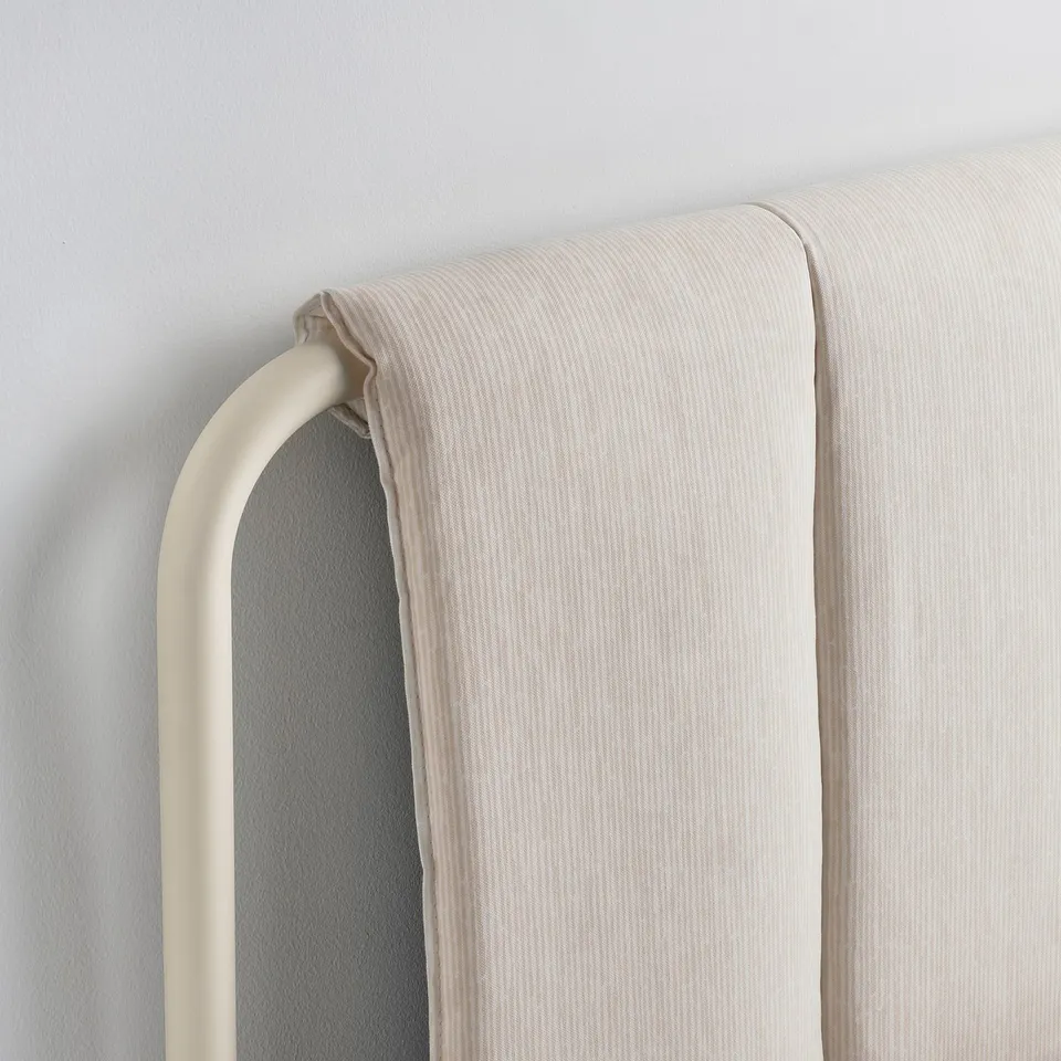 Modern beige bed frame detail. Soft, padded headboard with sleek metal support.