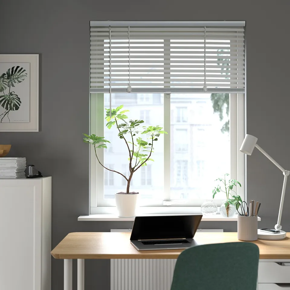 Modern office with VECKLARFLY blinds, desk, laptop, plant, green chair, grey walls, art, lamps.