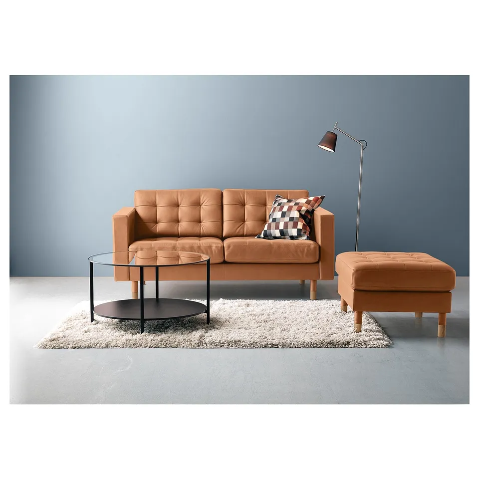 Modern living room setup: brown leather couch, round glass table, shaggy rug, blue wall, adjustable floor lamp.