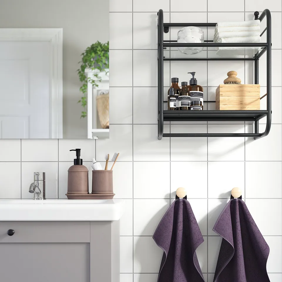 Modern bathroom with FRÖSJÖN wall shelf, holding towels & toiletries. Black metal frame, 2 tiers, glass shelving.