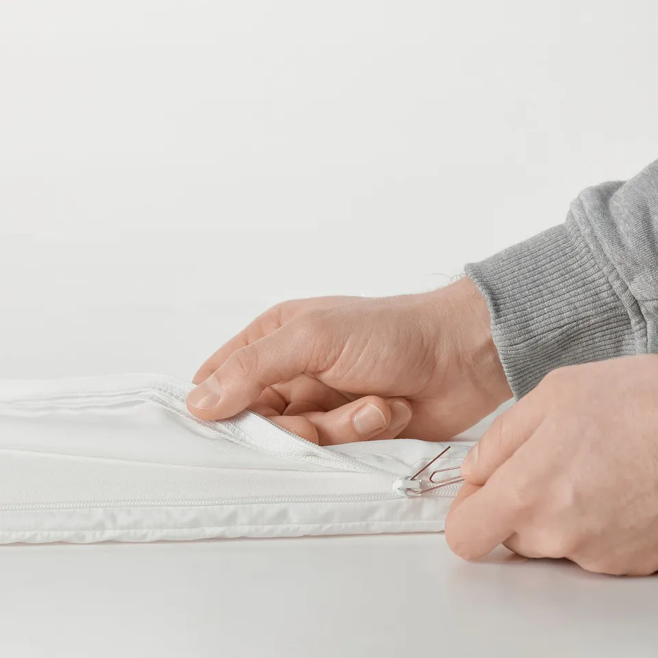 Hands zipping a mattress in a grey hoodie.