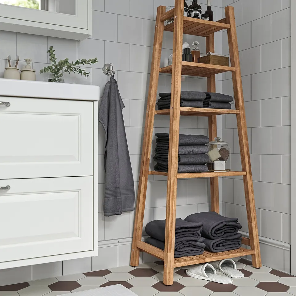 Natural wood STOREDAMM shelf near white cabinet, holding towels & toiletries.