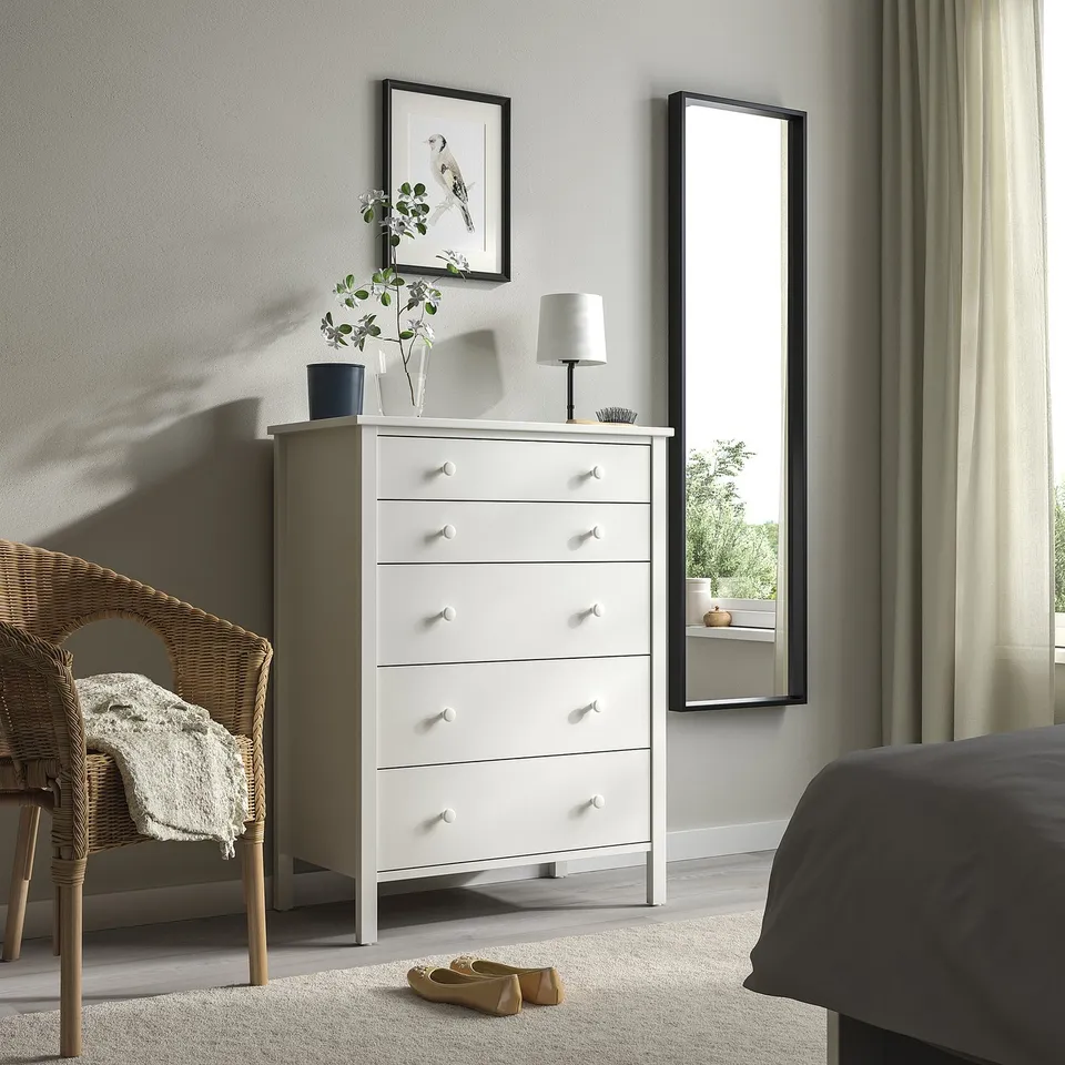 Minimalist bedroom with KILBERGET dresser, mirror, wicker chair, dark bed.