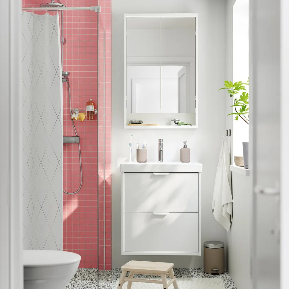 Minimalist bathroom with white drawers, mirror, & shower. Green plant & towel.