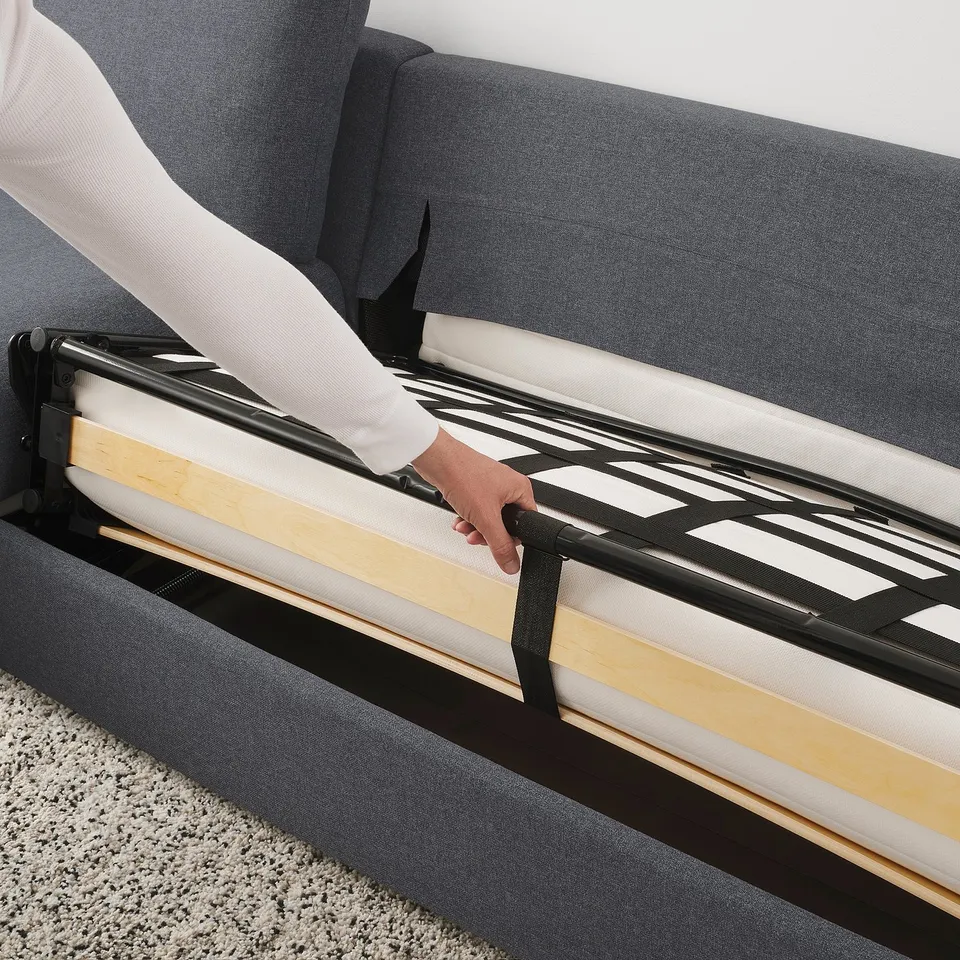 Person pulling out sofa bed, revealing a thick mattress on slatted frame.
