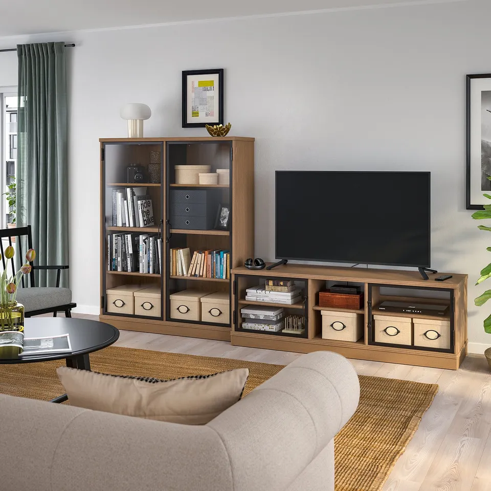 Modern living room with LANESUND tv bench, bookshelf, and neutral decor. Large tv, books, beige sofa, black coffee table, grey curtains.