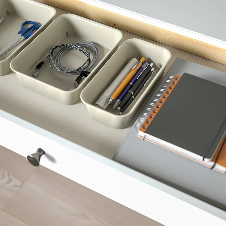 Organised desk with compartments: one storing coiled cables, another holding pens, and a notebook. Top drawer partially open, showing inner storage.