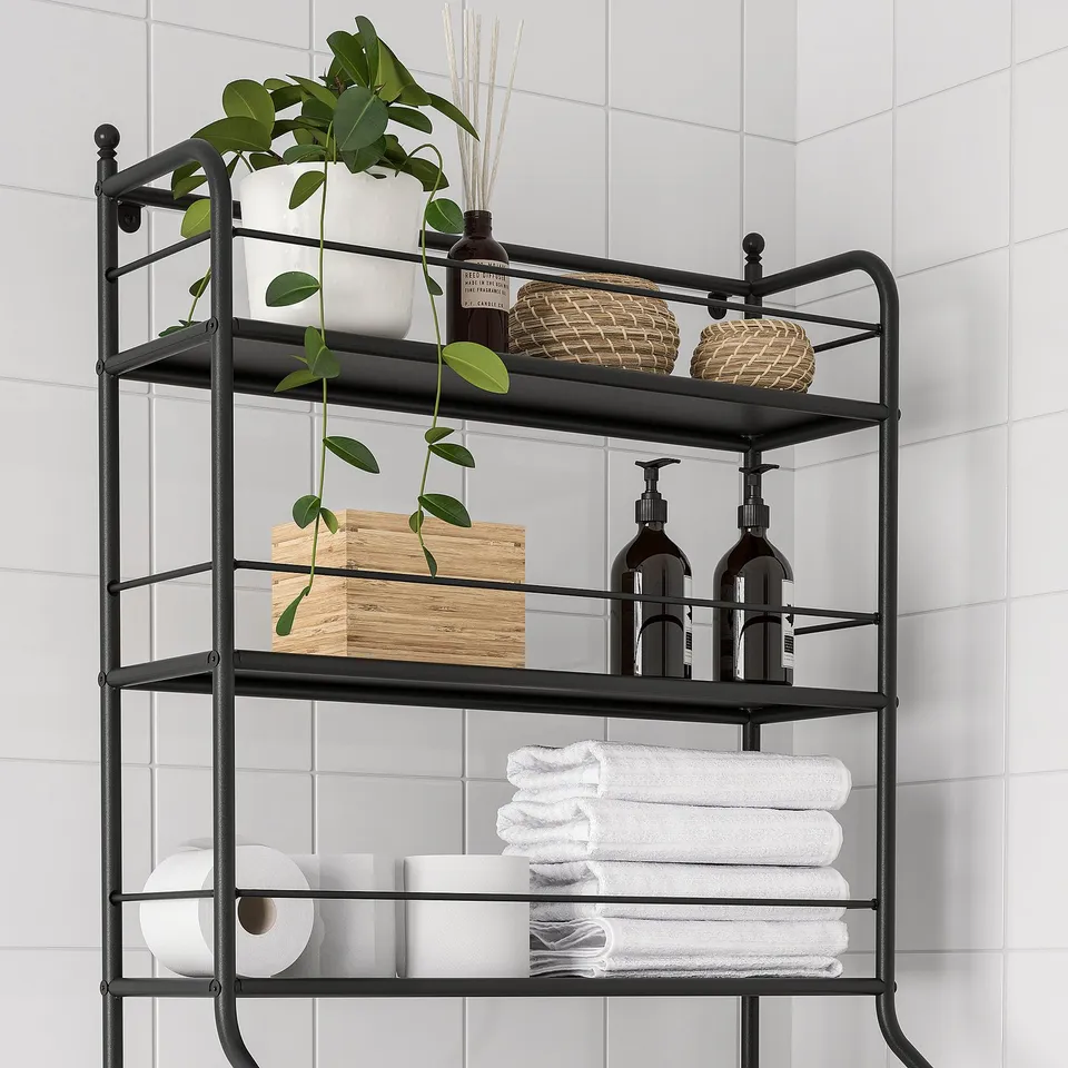 Black metal shelving unit over toilet with stacked towels, toilet paper, bottles, baskets, and a potted plant.