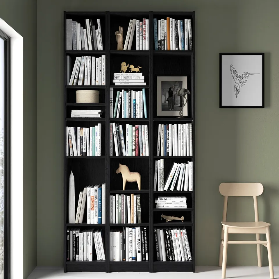 Black BILLY bookcase with books, art, & chair against green wall.