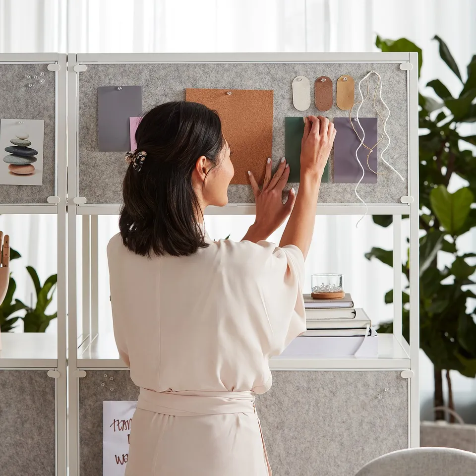 A person organises a TROTTEN double-sided cabinet with a notice board, featuring open and closed storage.