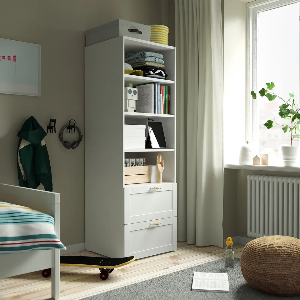 Grey and white SMÅSTAD bookcase with books, clothes, decor, a small bed, and framed art.