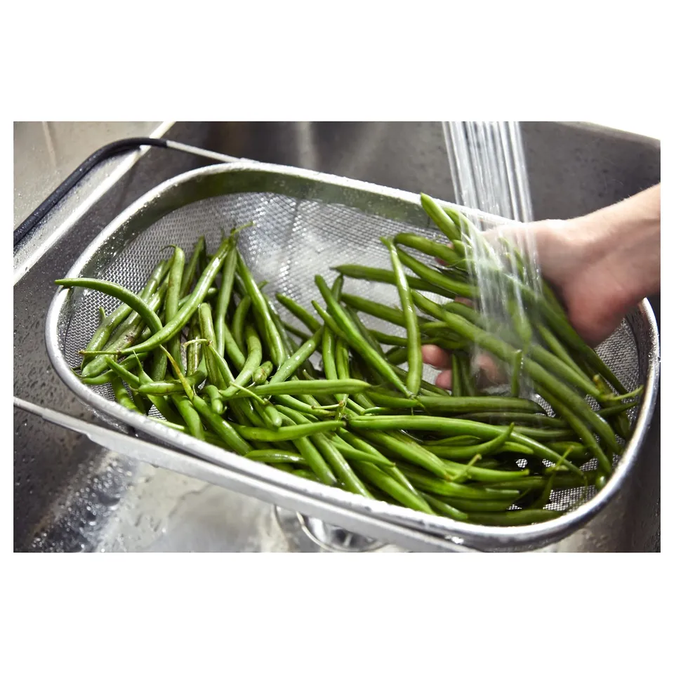 Person washing green beans in stainless steel sink strainer.