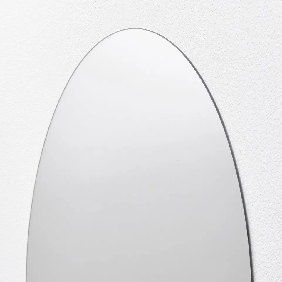 Large floor mirror with sleek frame, reflecting light softly, standing against white wall.