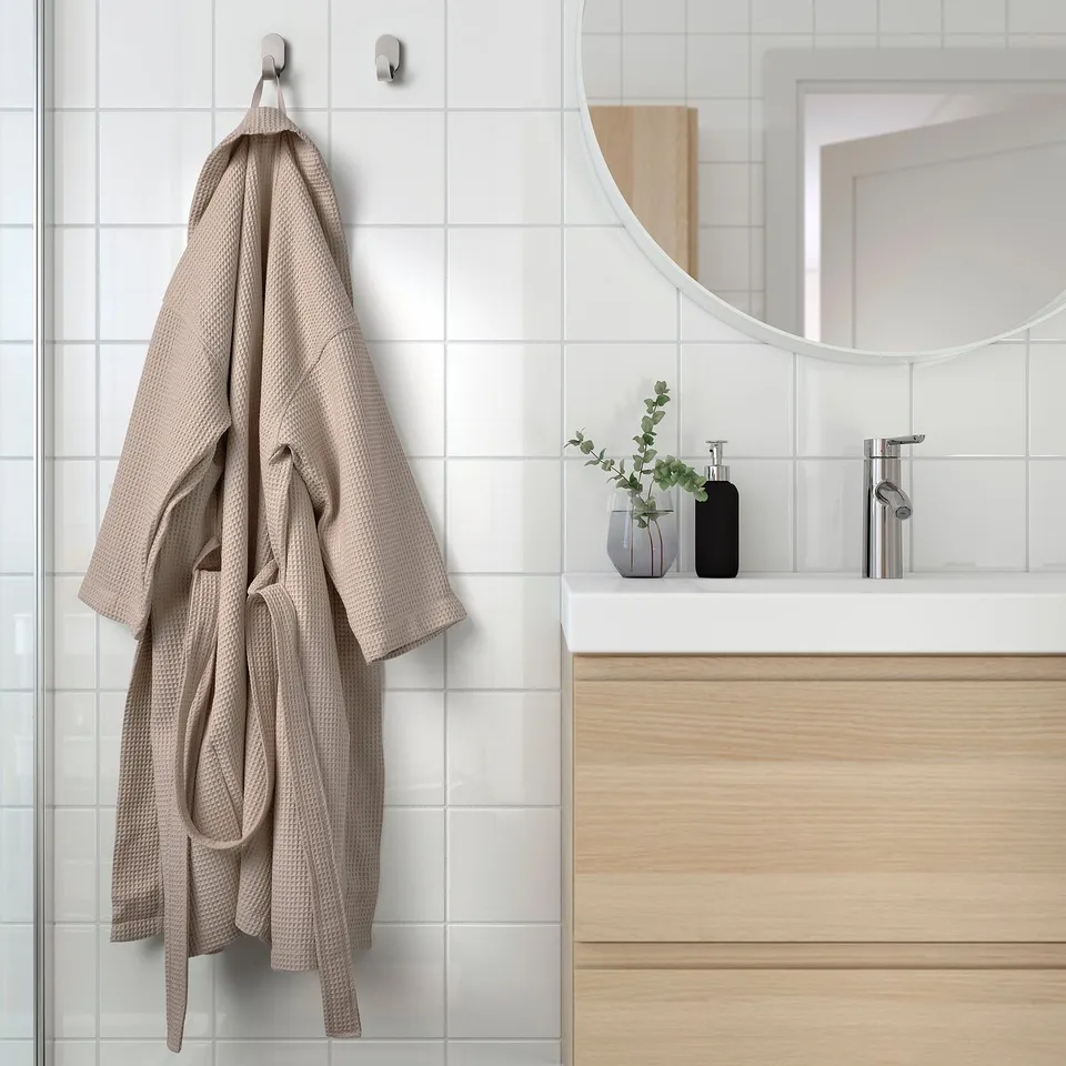 Beige robe with adjustable belt hangs on bathroom wall hook.
