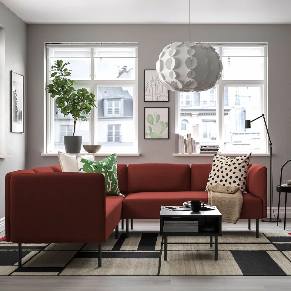 Modern living room with red sofa, green/white cushions, pendant light, rug, coffee table, lamp, wall art, and city view.
