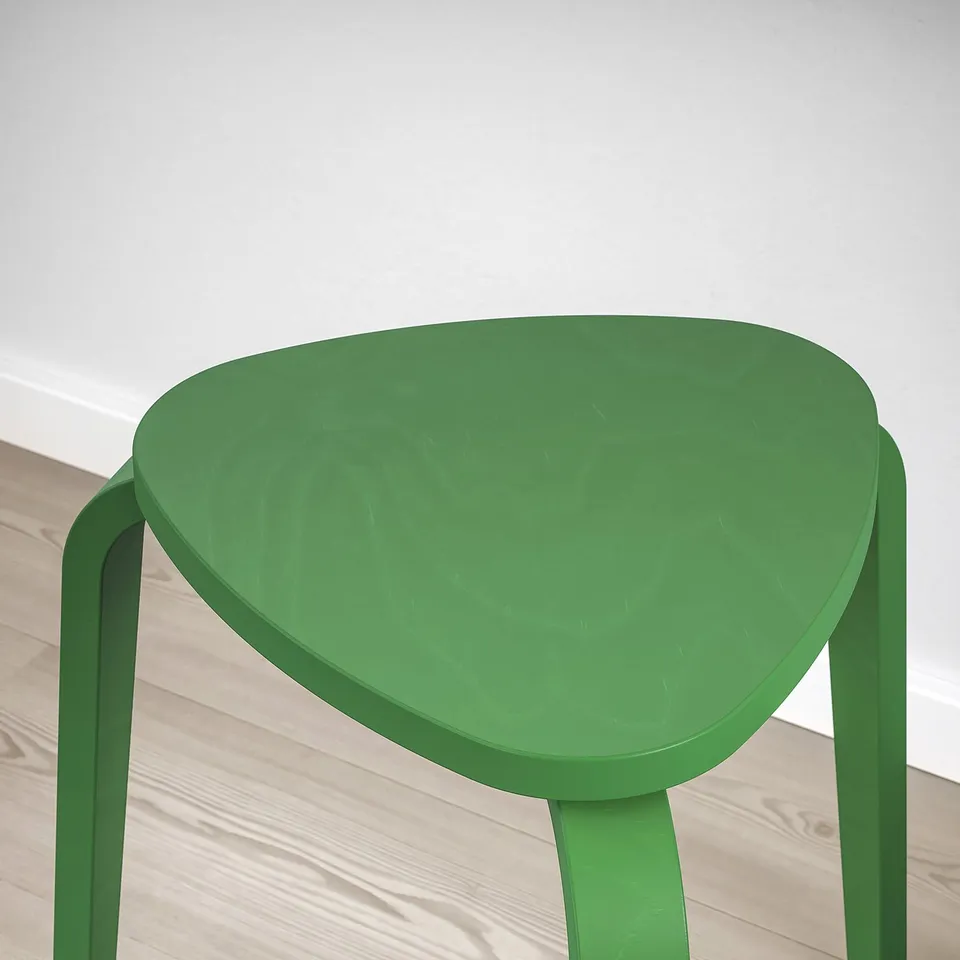 Green triangular stool with sturdy legs on wood floor.