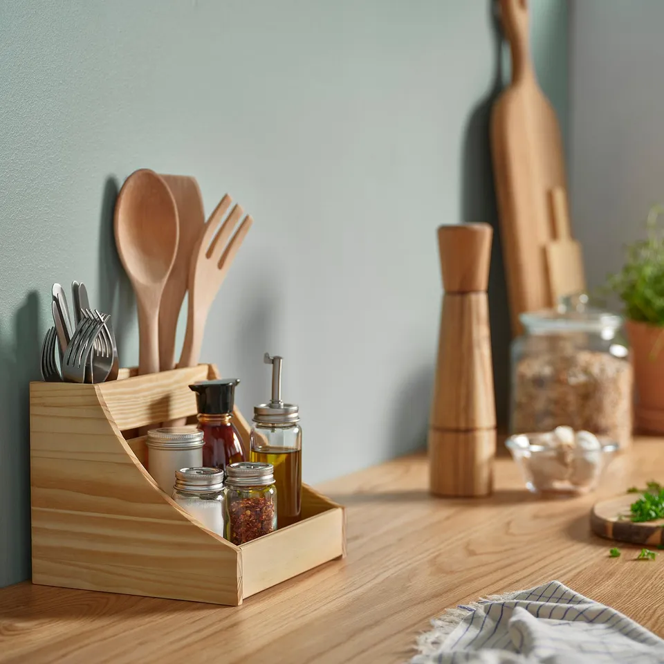 Kitchen counter with CHOKLADHAJ pine box holding utensils, spices, and bottles. Wooden pepper mill and herbs in background, neatly arranged.