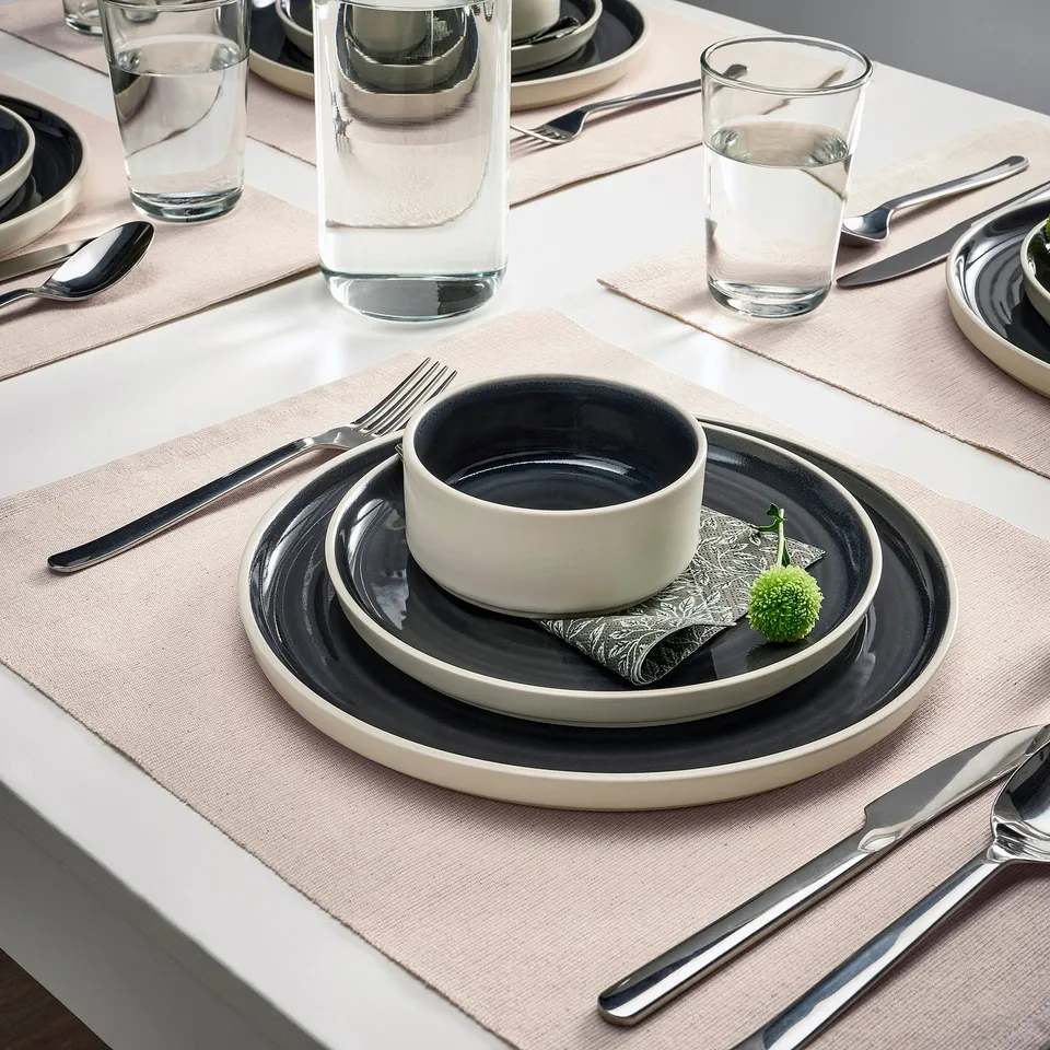 Table setting with SVARTSENAP place mats, featuring plates, cutlery, and glasses on light, protective mats.