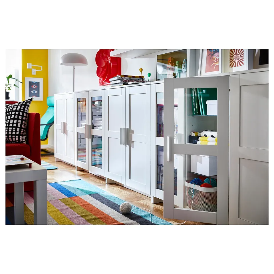 Bright, organised room with BRIMNES storage units. White cabinets, colourful rug, yellow wall, red chair.