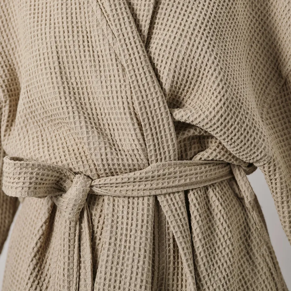 Close-up of a plush, beige robe with a waffle texture, tied with a belt.